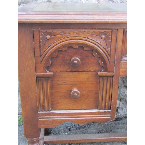 1191 - A reproduction oak writing table/desk with inset leather panel top over an arrangement of five friez... 