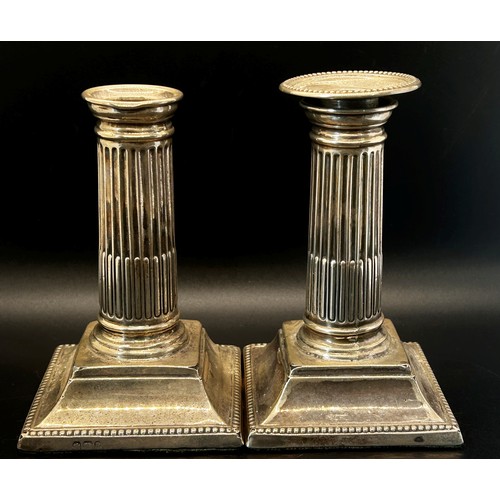 204 - A pair of small reeded silver column  candlesticks raised on a platform base (one lacking a sconce) ... 