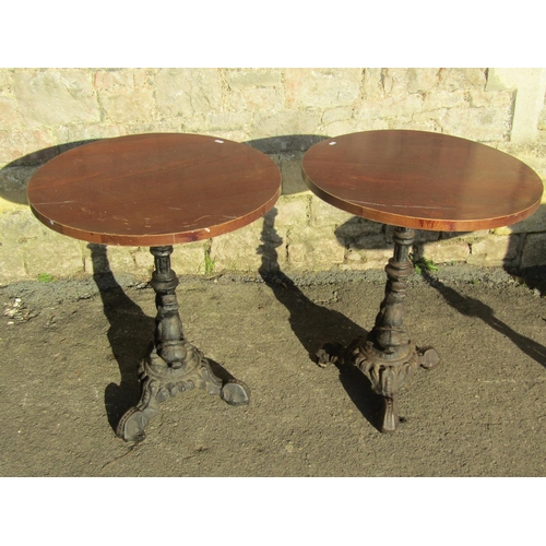 1071 - Pair of circular wooden topped pub tables raised on cast iron bases with entwined stylised dolphin d... 