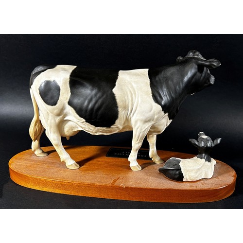 68 - A Beswick porcelain model of a Friesian cow & calf on oval timber base