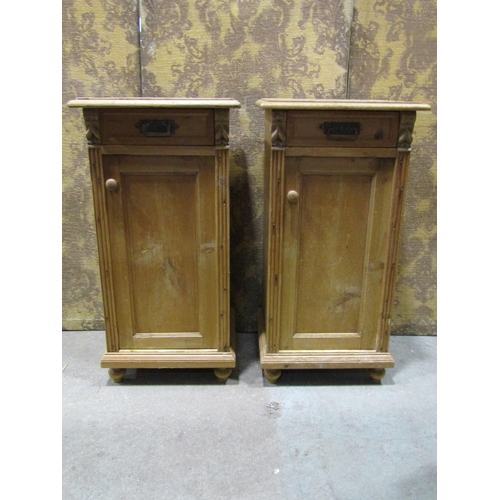 1075 - A pair of stripped and waxed pine bedside cabinets each enclosed by a panelled door and frieze drawe... 