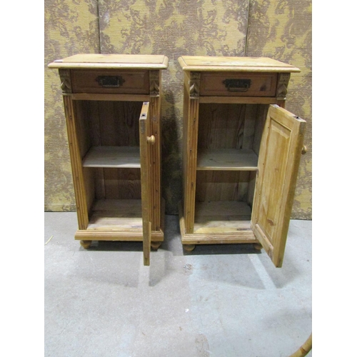 1075 - A pair of stripped and waxed pine bedside cabinets each enclosed by a panelled door and frieze drawe... 