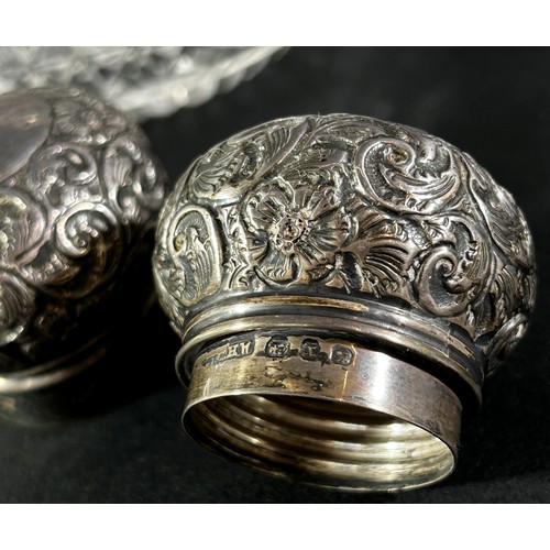 197 - A pair of cut glass dressing table bottles with silver floral engraved caps