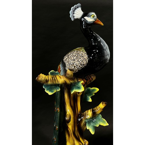 5 - A large ceramic figure of a majolica peacock set on a bough, with naturalistic colouring, 82cm high