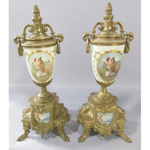 519 - A pair of brass urn shaped clock garnitures with a romantic pastoral scene, a circular tavern scene ... 