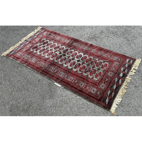 1493 - A Bokhara carpet with a central panel of red gul on a green ground 200cm x 100cm.