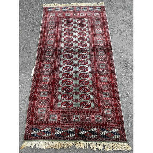 1493 - A Bokhara carpet with a central panel of red gul on a green ground 200cm x 100cm.