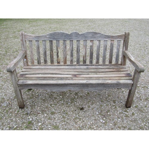 84 - A Bridgman weathered teak three seat garden bench with slatted seat and back beneath a shaped rail w... 