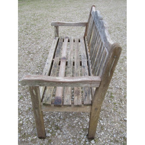 84 - A Bridgman weathered teak three seat garden bench with slatted seat and back beneath a shaped rail w... 