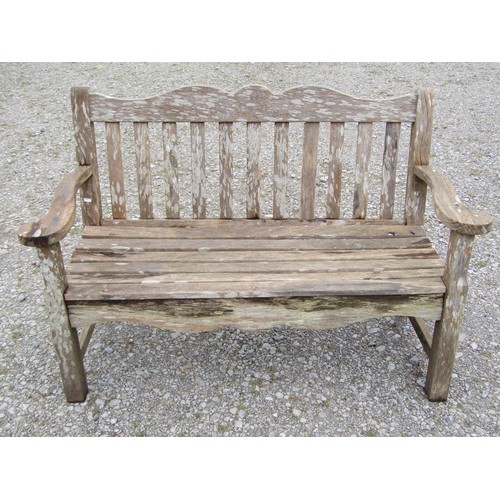 85 - A Bridgman two seat weathered teak garden bench with slatted seat and back beneath a shaped rail wit... 