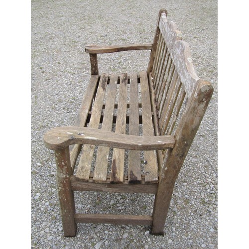 85 - A Bridgman two seat weathered teak garden bench with slatted seat and back beneath a shaped rail wit... 