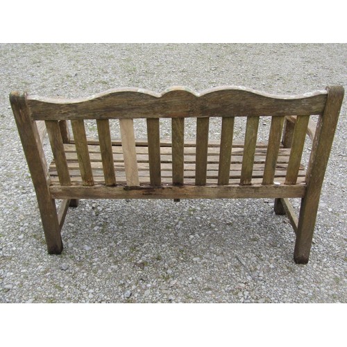 85 - A Bridgman two seat weathered teak garden bench with slatted seat and back beneath a shaped rail wit... 