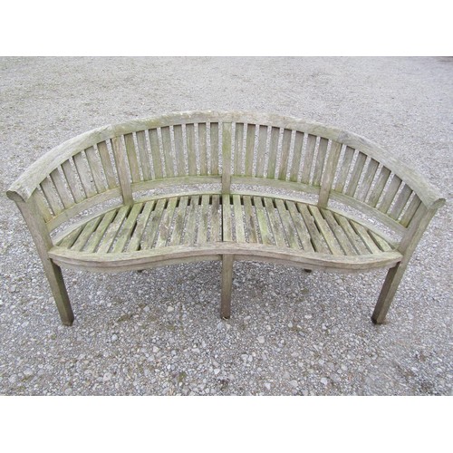 74 - A pair of weathered teak banana shaped garden benches with loose seat cushions, 160 cm wide