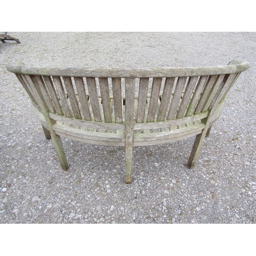 74 - A pair of weathered teak banana shaped garden benches with loose seat cushions, 160 cm wide