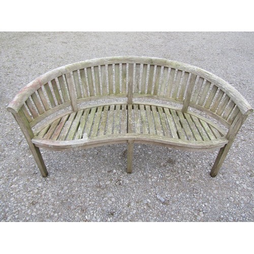 74 - A pair of weathered teak banana shaped garden benches with loose seat cushions, 160 cm wide