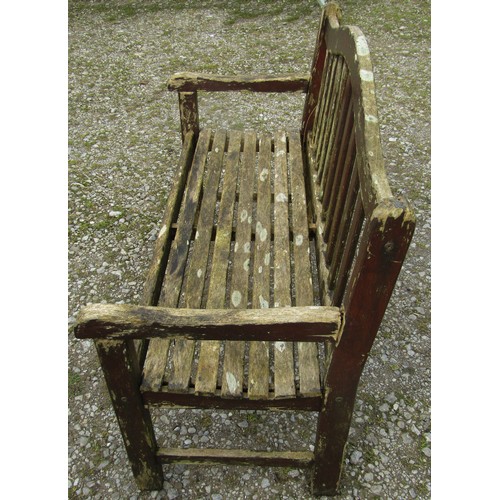 111 - A weathered and stained teak garden bench with slatted seat and back beneath an arched rail, 120 cm,... 