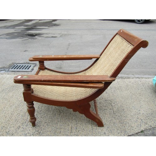 543 - An early 20th century teak plantation chair, with curved woven rattan seat and folding / extending a... 