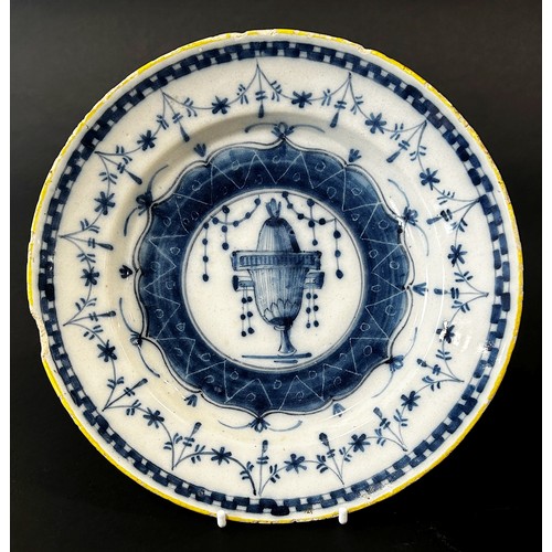 21 - An 18th century tin glazed plate in a blue and white colourway, the central urn within further geome... 