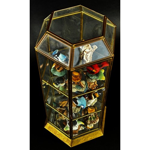 39 - A collection of twelve mini bisque birds within three tier brass frame cabinet of hexagonal form