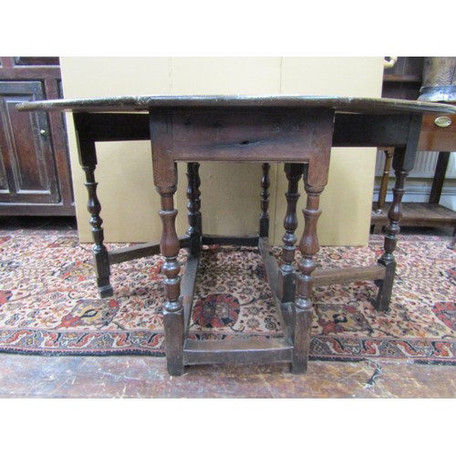 1141 - An 18th century oak and fruitwood gateleg table enclosing a single frieze drawer on turned supports,... 