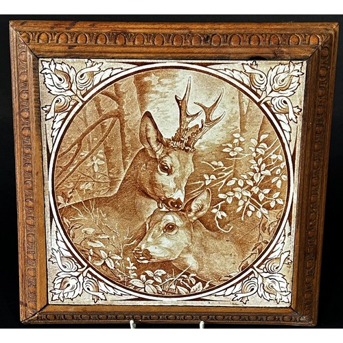 29 - A decorative ceramic tile mounted in a wooden frame as a trivet, depicting a pair of roe deer in sep... 