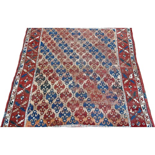 1486 - An old Persian rug with diagonal red and blue geometric patterns, worn in places, 163cm x 136cm appr... 