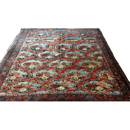 1512 - An Old Persian carpet with a repeating floral pattern on a pink ground, one corner badly worn with m... 