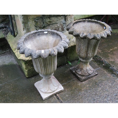 1132 - A pair of weathered cast composition stone garden urns with trumpet shaped foliate bowls set on a fi... 