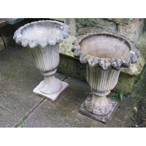 1132 - A pair of weathered cast composition stone garden urns with trumpet shaped foliate bowls set on a fi... 