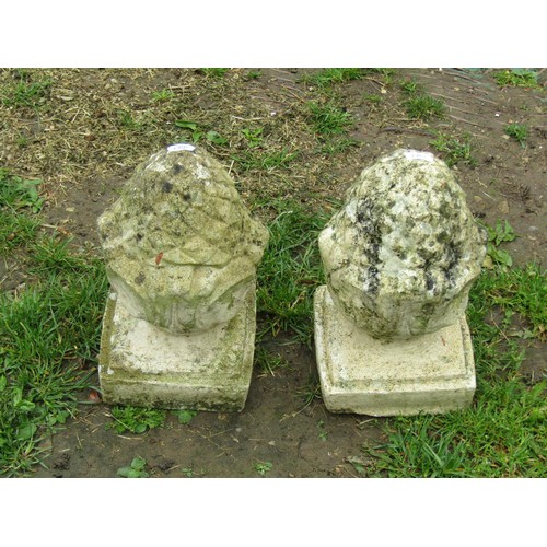 1138 - A pair of small weathered cast composition stone pineapple pier finials with fixed square stepped ba... 