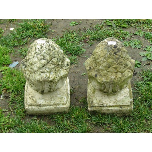 1138 - A pair of small weathered cast composition stone pineapple pier finials with fixed square stepped ba... 