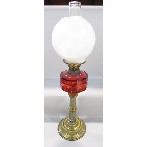 556 - A Victorian brass column oil lamp with a cracked cranberry red font and an opaque shade, together wi... 