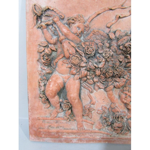 570 - A Terracotta wall plaque of four putti in relief frolicking amongst garlands of flowers, bearing a s... 