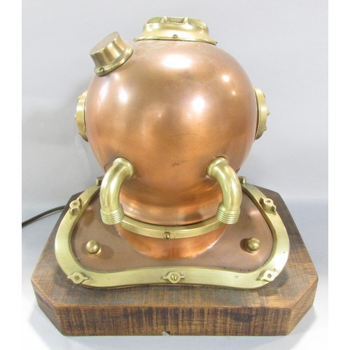 522 - A decorative table lamp in the form of a small copper and brass diver’s helmet raised on a wooden pl... 