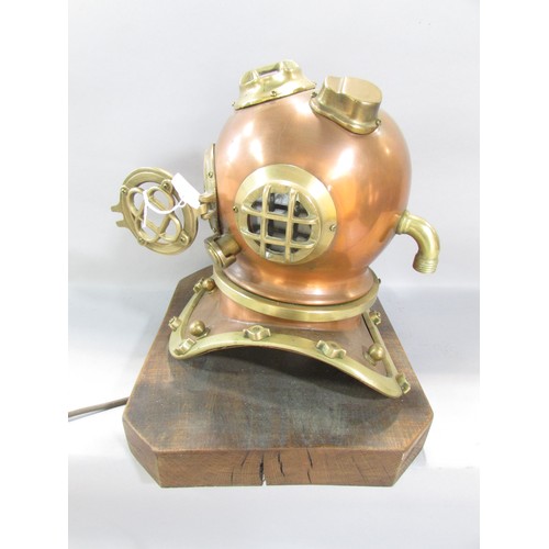 522 - A decorative table lamp in the form of a small copper and brass diver’s helmet raised on a wooden pl... 