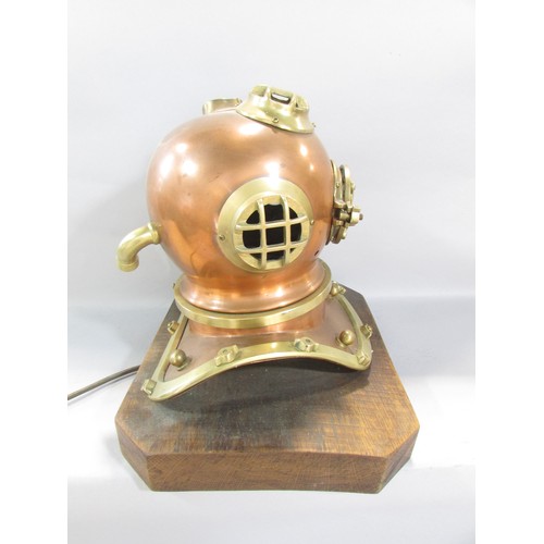 522 - A decorative table lamp in the form of a small copper and brass diver’s helmet raised on a wooden pl... 