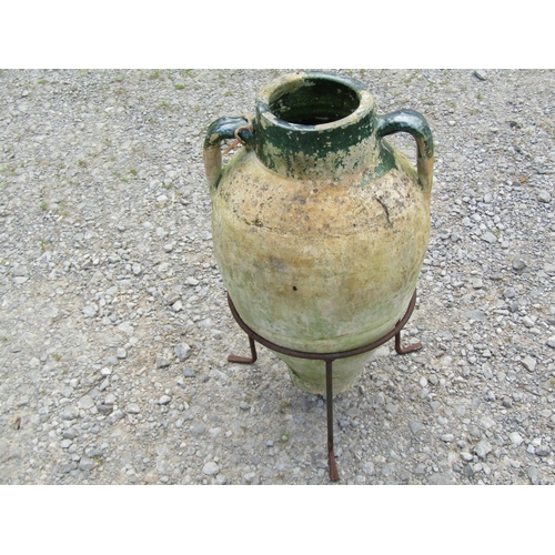 1024A - A weathered clay amphora with moulded loop handles and green glazed neck set in simple iron stand, 6... 