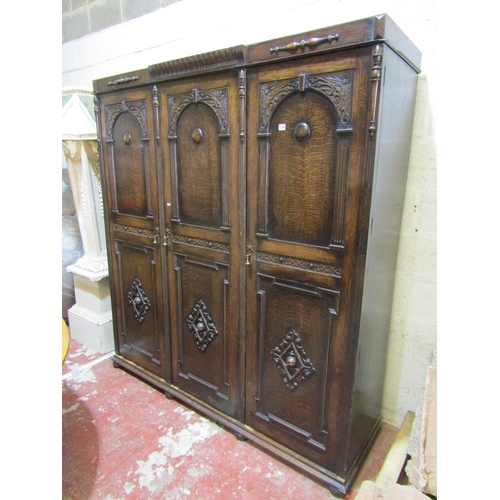 1706 - A 1920s Jacobean revival oak triple wardrobe enclosed by three panelled doors with geometric and fur... 