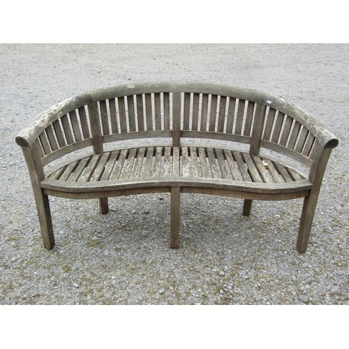 1151 - A weathered teak banana shaped garden bench with slatted seat and back, 160 cm long