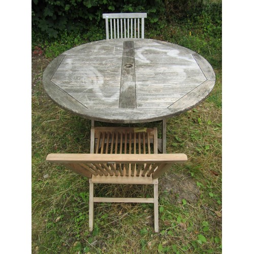 1157 - A weathered circular folding teak garden table with slatted panelled top, 120cm diameter together  w... 