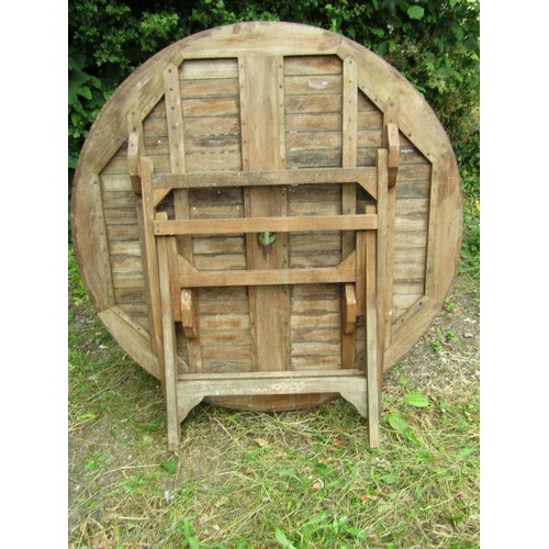 1157 - A weathered circular folding teak garden table with slatted panelled top, 120cm diameter together  w... 