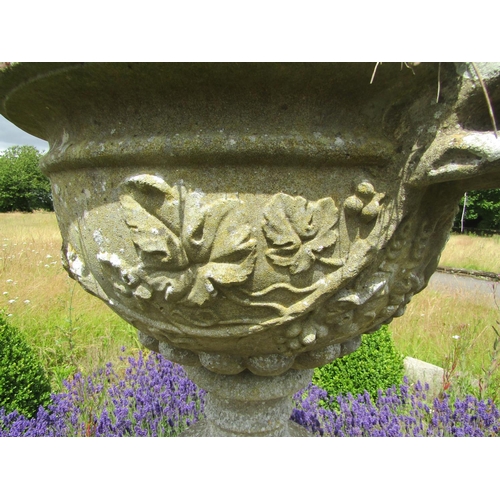 1068 - A weathered composition stone twin-handled urn shaped planter with moulded fruiting vine detail, rai... 