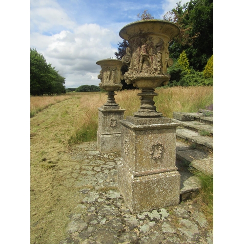 1097 - A monumental pair of 19th century weathered composition stone garden urns, raised on associated plin... 