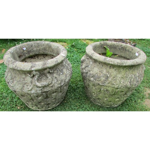 1020 - A pair of weathered cast composition stone garden urns with repeating relief detail and fixed ring h... 