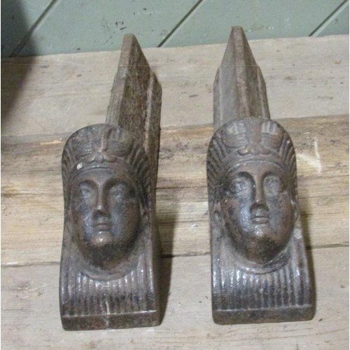 1107 - A pair of 19th century fire dogs, with stylised mask mounts in the Egyptian style, each 40cm long.