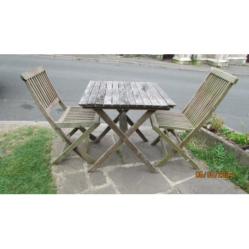 1043 - A weathered teak garden terrace table with slatted top, 70 cm square raised on folding x framed supp... 