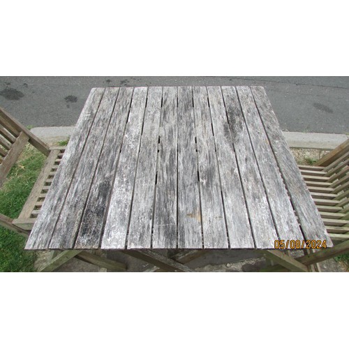 1043 - A weathered teak garden terrace table with slatted top, 70 cm square raised on folding x framed supp... 