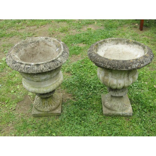 1066 - Two similar weathered composition stone garden urns with flared rims and lobbed bodies raised on loo... 