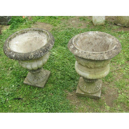 1066 - Two similar weathered composition stone garden urns with flared rims and lobbed bodies raised on loo... 