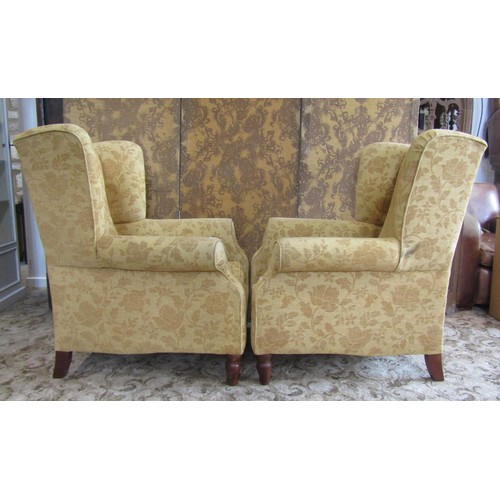 1350 - A matched pair of Georgian style upholstered wing armchairs, with golden floral covers raised on tur... 